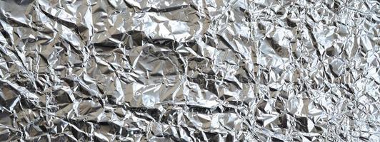 Thin wrinkled sheet of crushed tin aluminum silver foil background with shiny crumpled surface for texture photo