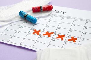Menstrual pads and tampons on menstruation period calendar with red cross marks lies on lilac background photo