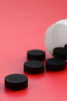 Several black tablets fall out of the plastic jar on the red surface. Background image on medical and pharmaceutical topics. Activated Charcoal photo