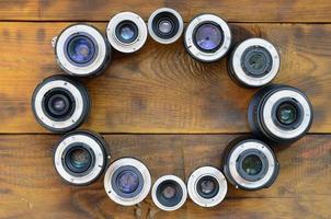 Several photographic lenses lie on a brown wooden background. Space for text photo