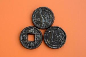 Three chocolate products in the form of Euro, USA and Japan coins lie on an orange plastic background. A model of cash coins in an edible form photo