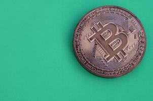 Chocolate product in the form of physical bitcoin lies on a green plastic background. Model of the crypto currency in the edible form photo