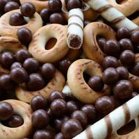 A lot of crispy sweet tubules, chocolate melting balls and yellow bagels lie on a wooden surface. Close up view photo