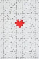 The texture of a white jigsaw puzzle in an assembled state with one missing element forming a red space photo