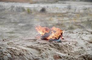 Burning sports sneakers or gym shoes on fire stand on sandy beach coast. Athlete burned out. Physical exertion during training concept photo