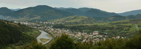 A beautiful view of the village of Mezhgorye, Carpathian region. A lot of residential buildings surrounded by high forest mountains and long river photo