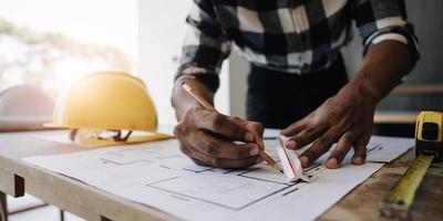 Image of engineer drawing a blue print design building or house, An engineer workplace with blueprints, pencil, protractor and safety helmet, Industry concept photo