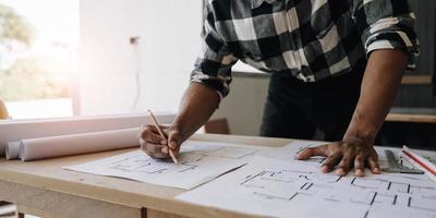 Image of engineer drawing a blue print design building or house, An engineer workplace with blueprints, pencil, protractor and safety helmet, Industry concept photo