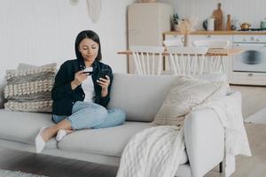 mujer con tarjeta de crédito, teléfono usando servicios bancarios en línea, sentada en el sofá, comprando en casa foto