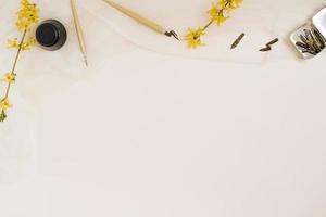 Calligraphy, sharp pen, ink, quills, yellow forsythia flower on beige background with copying space photo