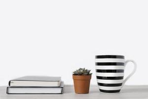 A mug with white and black stripes and notepads and a small pot of succulent with a pot of spoons on the office table. Copy space, front view photo