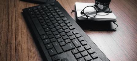 Banner closeup of wood desk with keyboard, glasses and notebook. Work from home. Technology keyboard with copy space. photo