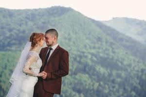 feliz novia y novio corriendo y divirtiéndose en las montañas en un día soleado de verano. hermosa pareja de recién casados riendo, verdaderos sentimientos. momento romántico emotivo. foto