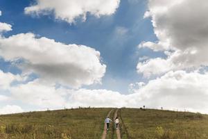 Loving young happy couple running on a green meadow with blue cloudy sky on the background. selective focus photo