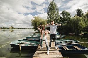 young couple in love having fun with oars on the wooden bridge. stylish woman and man enjoy canoeing on sunny lake. photo