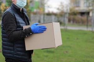 Delivery man in face medical mask, gloves hold empty cardboard box outdoors. Service coronavirus. Online shopping. mock up. photo