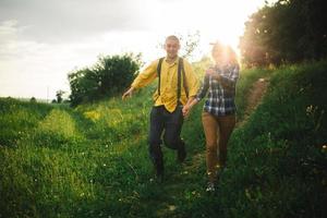 amorosa pareja hipster caminando en el campo, besándose y tomándose de la mano, abrazándose, tumbada en la hierba en el verano al atardecer. día de San Valentín foto