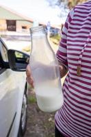 la mano sostiene una botella de leche cruda de la granja, que está casi borracha, contra el fondo de un granero