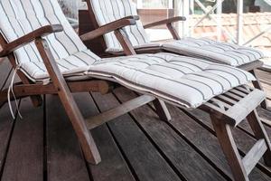 Empty wooden deck chair with a soft pillow on the terrace, against the background of the roofs. photo