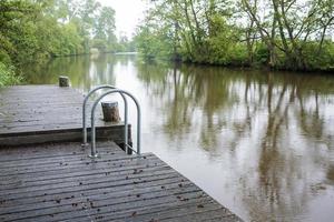 Wooden pier with a metal ladder for easy entry into the water, on the river. Rural landscape. photo