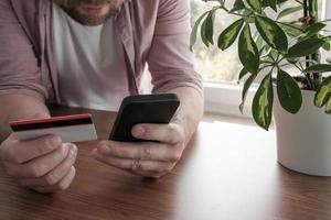 el hombre europeo realiza un pago en línea con una tarjeta de crédito y un teléfono inteligente. foto