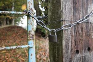 Padlock and chain linking an old metal gate and a wooden pole with barbed wire, blocking the passage to a private area. photo