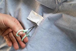 la mano corta la etiqueta de instrucciones con tijeras en una camisa nueva, gris. copie el espacio plano foto