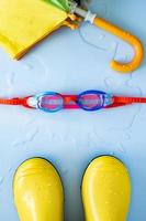 Rubber boots, a umbrella and swimming goggles on a blue background in a puddle of water. Concept of preparation for the rainy season. photo