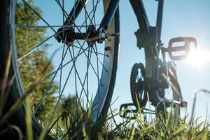 detalle de primer plano de una bicicleta estacionada en un prado, contra el telón de fondo del sol y el cielo azul. concepto de estilo de vida activo. vista inferior. foto