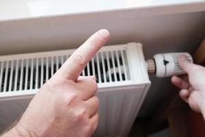 Forefinger makes a cautionary gesture and reminds of economy, against the background of a radiator. photo