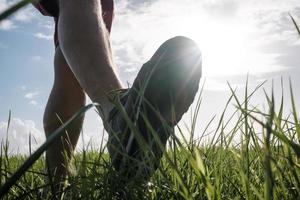 Foot in sneakers walks along a meadow, against the backdrop of the sun and sky. Active lifestyle and vacation concept. Bottom view. photo