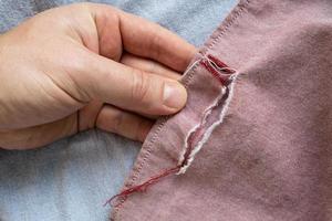 Torn new shirt, pink. Hand is holding a garment with a hole. Flatley. photo