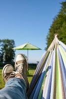 piernas masculinas en zapatillas y jeans en una hamaca, en un cálido día de verano, acampando. estilo de vida. foto