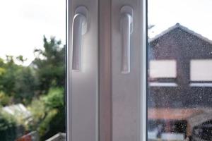 Closed white PVC window with two sashes, with dirty glass, through which the courtyard is visible. Close-up. photo