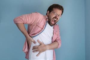 Young man is experiencing severe pain in the abdominal cavity, he holds on to the sore spot with hands and screams. photo