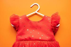 Beautiful baby red dress on a white clothes hanger, on an orange background. Top view. photo