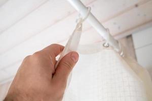 Hand closes a waterproof curtain in the bathroom, which covers the shower and prevents moisture from entering the floor. Bottom view. photo