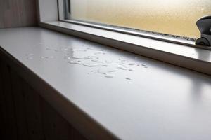 Accidentally spilled water on white window sills, against the background of a window and glass with condensation, indoors. photo