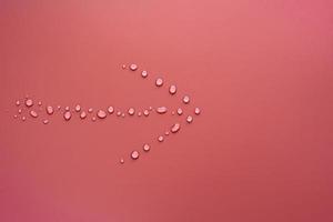 Arrow from drops of pure water, on a pink background. Sign showing the way. Copy space. Top view. photo