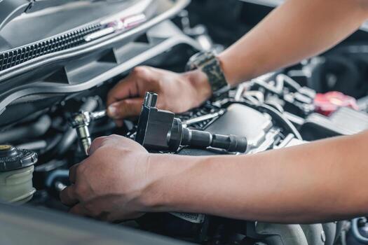 Close up spark plug coil on engine cover and a man use block wrench remove a bolt for take off coil engine service in garage and engine room  background photo