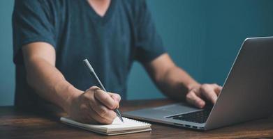 concepto de aprendizaje electrónico. hombre de negocios casual que estudia un curso en línea a través de una computadora portátil y escribe en un cuaderno. foto