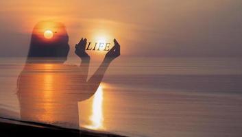 Human healthy Life balance concept, Woman holding sun in hands with LIFE character text at sunrise on the beach.