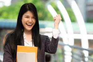 Young Asian woman holding books and smiling raised fist hand in the university, people education concept. photo