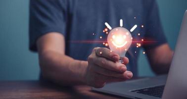 Hand of a man holding a light bulb with happy smile face and using a laptop computer. The idea of inspiration from online technology, innovation idea concept. photo
