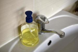 A shiny faucet with water and a washbasin with liquid soap in the room. A place for washing and soap. photo