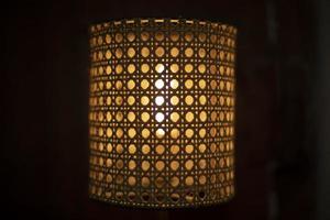 Lamp in dark. Wooden lampshade around incandescent lamp. photo