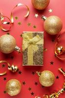 flat lay composition with gold giftbox, serpentine streamers and Christmas baubles on red background. Festive greeting card photo