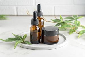 Cannabis face cream and serum or oil dropper concept. Natural cosmetic. CBD oil, THC tincture and hemp leaves on a marble table. photo