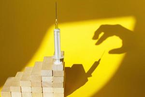 shadow of a man's hand about to steal a syringe with a vaccine on yellow background photo