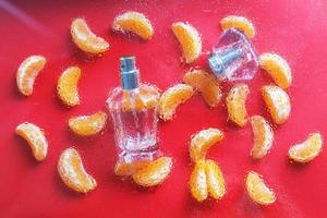 Frasco de perfume para mujer de fondo rojo, decorado con rodajas de mandarina. el concepto de un perfume cítrico fresco foto